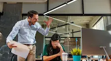 Angry man standing over a women with her head in her hands while he shouts at her