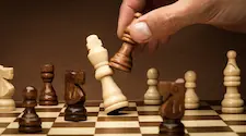 Wood chesss board with the king being toppled by a pawn