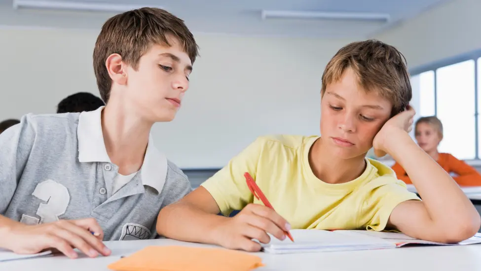 boy leaning over the shoulder of another boy to copy their work