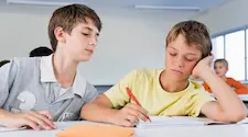 boy leaning over the shoulder of another boy to copy their work