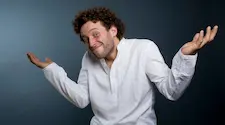 Man in white share with outstretched arms shrugging his shoulders