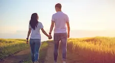 rear view of two people holding hands walking on a path amongst long grass