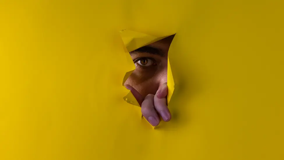 man peaking through a teared hole in a sheet of yellow paper