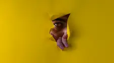man peaking through a teared hole in a sheet of yellow paper