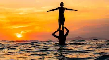 standing on the shoulders of a person in the sea with a golden sunset