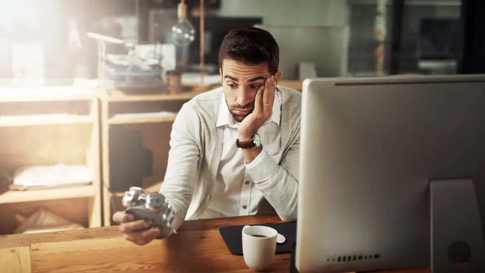 Perplexed man sitting in front of computer holding an alarm clock